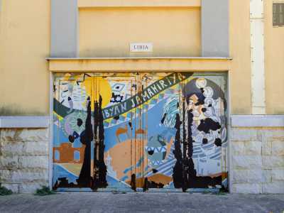 Una porta mostra un paesaggio tipicamente africano: un fiammeggiante disco solare, dune di sabbia, cammelli, il mar Mediterraneo sullo sfondo. Stiamo ammirando Porta Libia, realizzata dall�artista Salaheddin Mansur Zagruna. Il lato destro della composizione � interamente occupato dall�immagine di una donna con indosso collane e amuleti